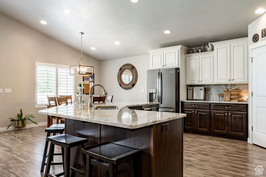 Kitchen with stainless steel refrigerator with ice dispenser, a breakfast bar, wood finished floors, recessed lighting, and a kitchen island with sink