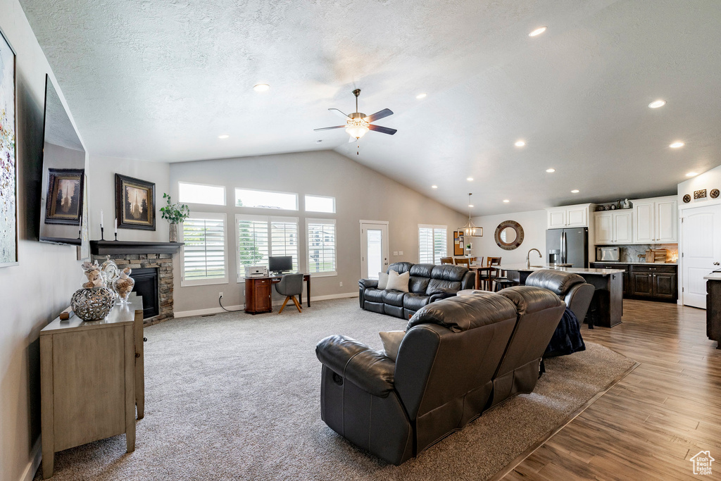 Living room with ceiling fan, a stone fireplace, vaulted ceiling, recessed lighting, and wood finished floors