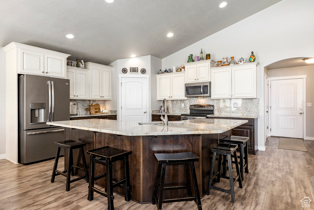 Kitchen featuring stainless steel appliances, arched walkways, white cabinetry, backsplash, and recessed lighting