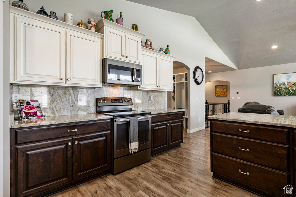 Kitchen featuring appliances with stainless steel finishes, arched walkways, dark brown cabinets, white cabinets, and vaulted ceiling