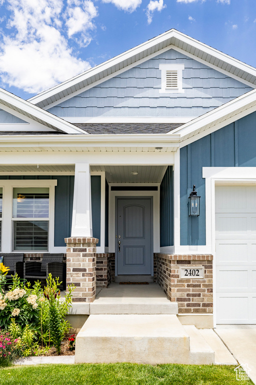 View of exterior entry with brick siding, a porch, a garage, and board and batten siding