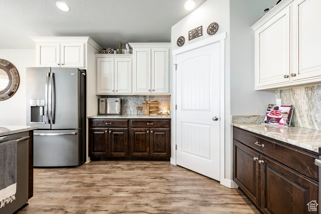 Kitchen with stainless steel fridge, range, white cabinetry, dark brown cabinets, and tasteful backsplash