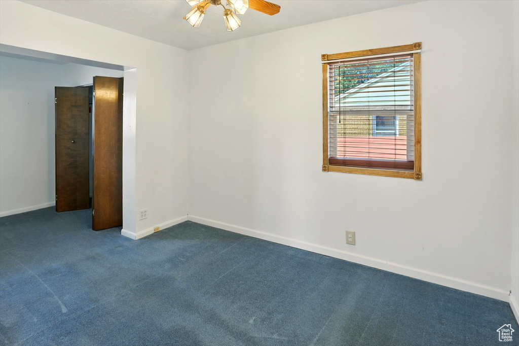 Spare room with ceiling fan and dark colored carpet