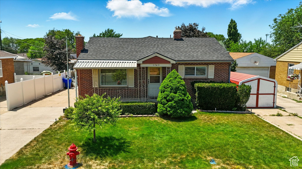 Bungalow-style house with a chimney, brick siding, a shed, and a shingled roof