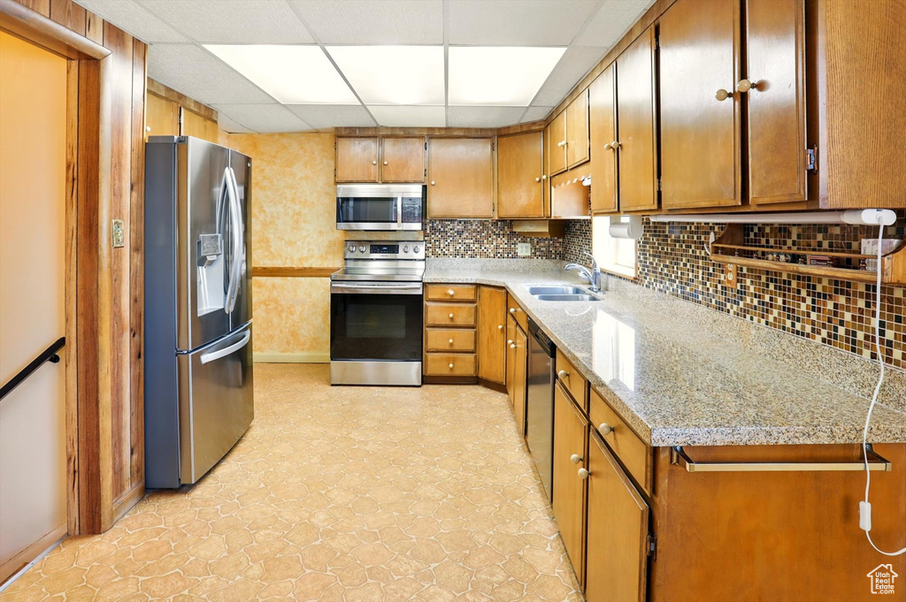 Kitchen with stainless steel appliances, a drop ceiling, brown cabinets, and decorative backsplash
