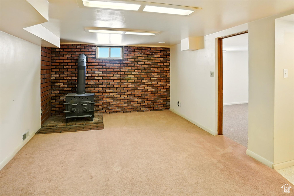 Unfurnished living room featuring carpet flooring, a wood stove, and brick wall