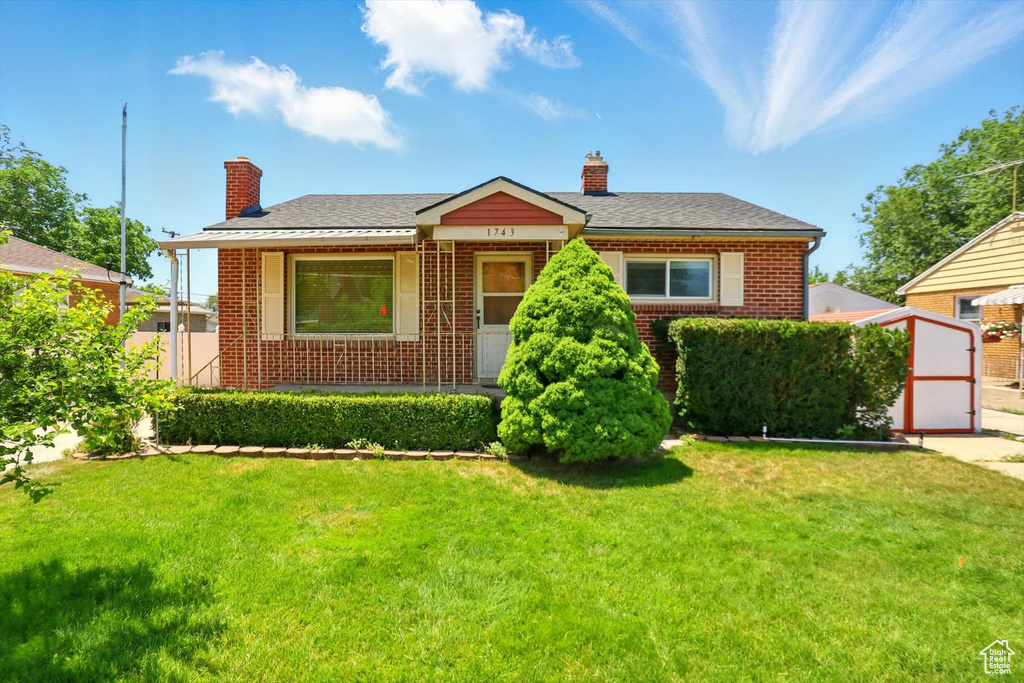 View of front of property with brick siding, a chimney, a front lawn, and an outdoor structure