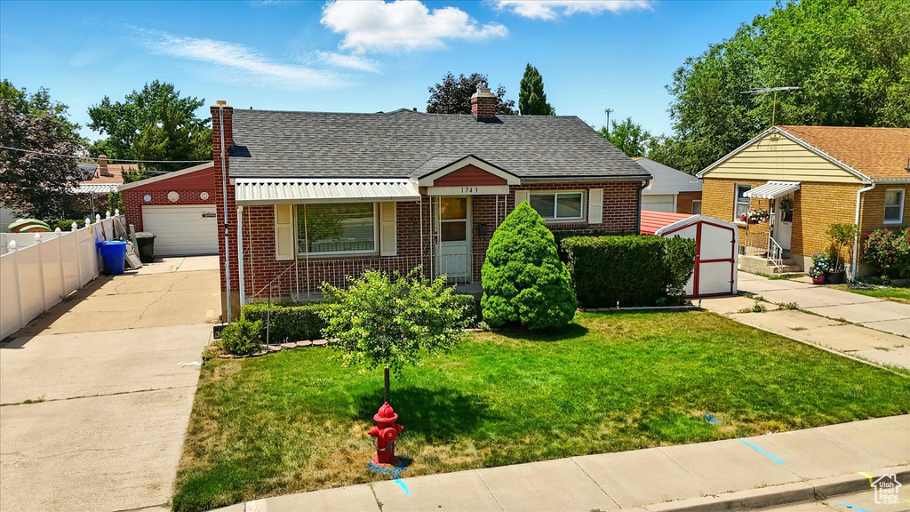 Bungalow-style home featuring brick siding, a chimney, a detached garage, roof with shingles, and an outbuilding