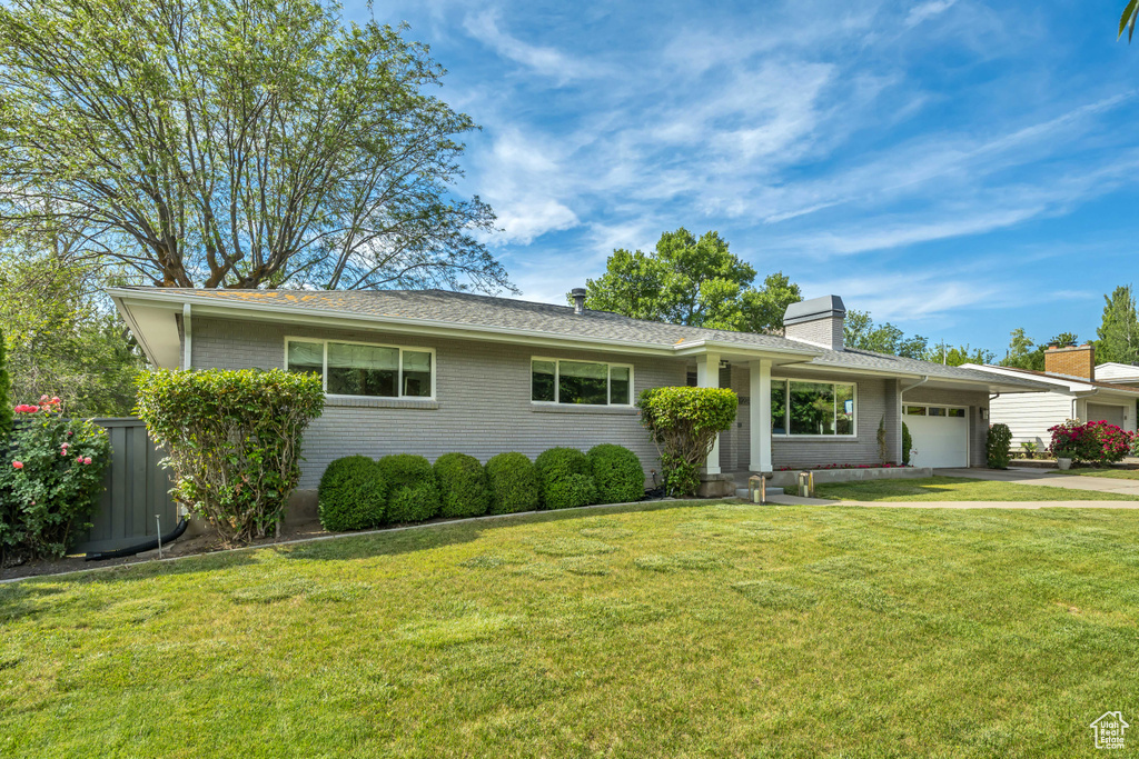 Ranch-style house featuring an attached garage, driveway, a front lawn, and a chimney