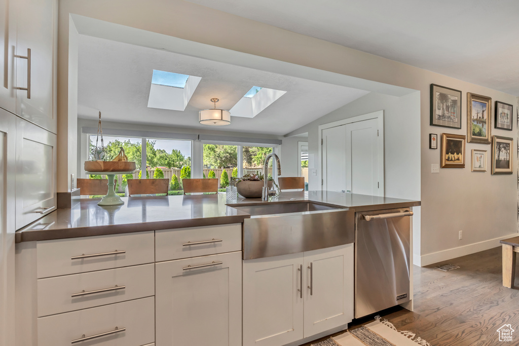Kitchen featuring dishwasher, a skylight, wood finished floors, white cabinetry, and vaulted ceiling
