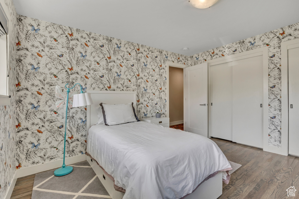 Bedroom with wood finished floors, wallpapered walls, and a closet