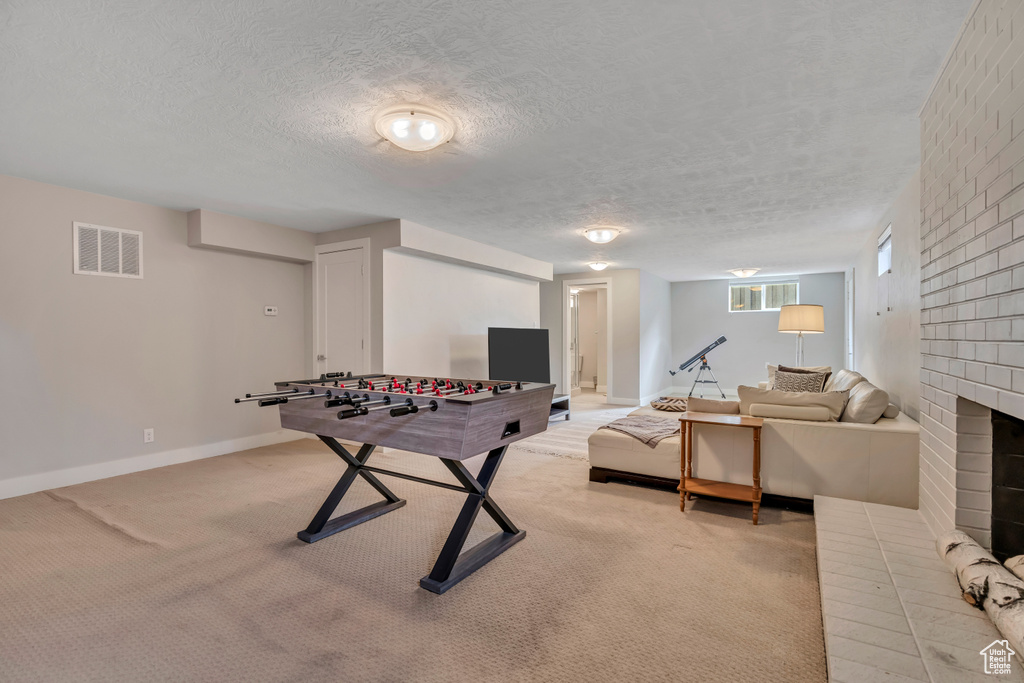 Game room featuring light colored carpet, a brick fireplace, and a textured ceiling