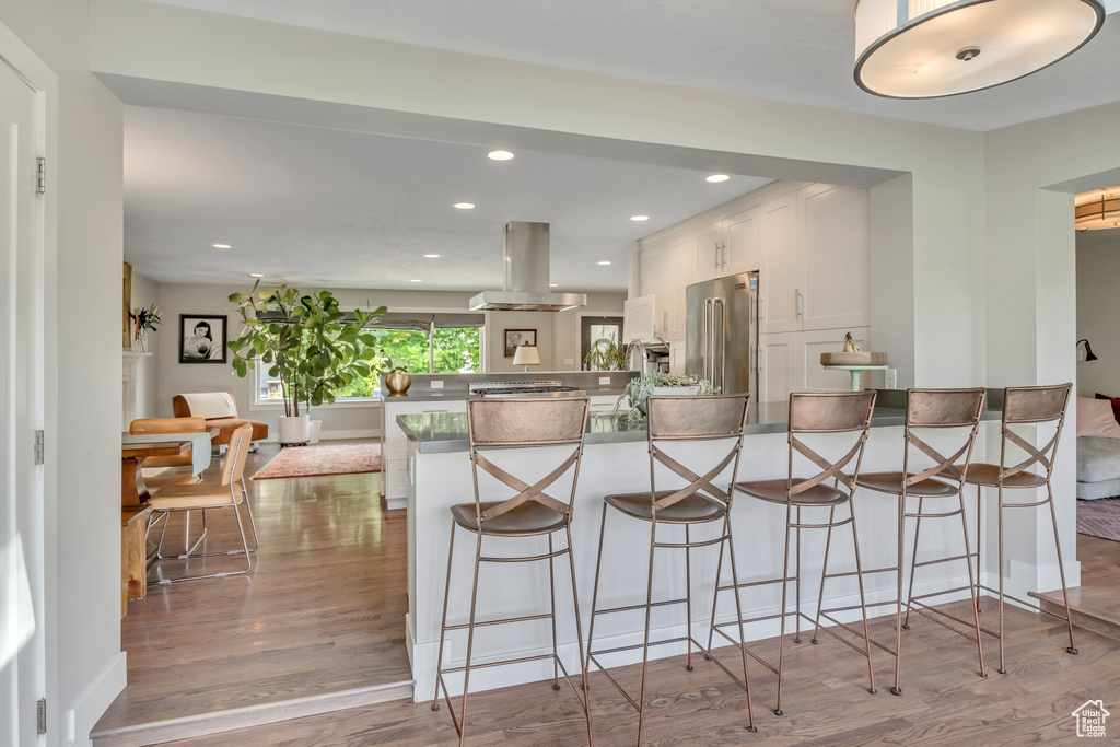 Kitchen with island exhaust hood, a peninsula, high end fridge, white cabinetry, and a breakfast bar