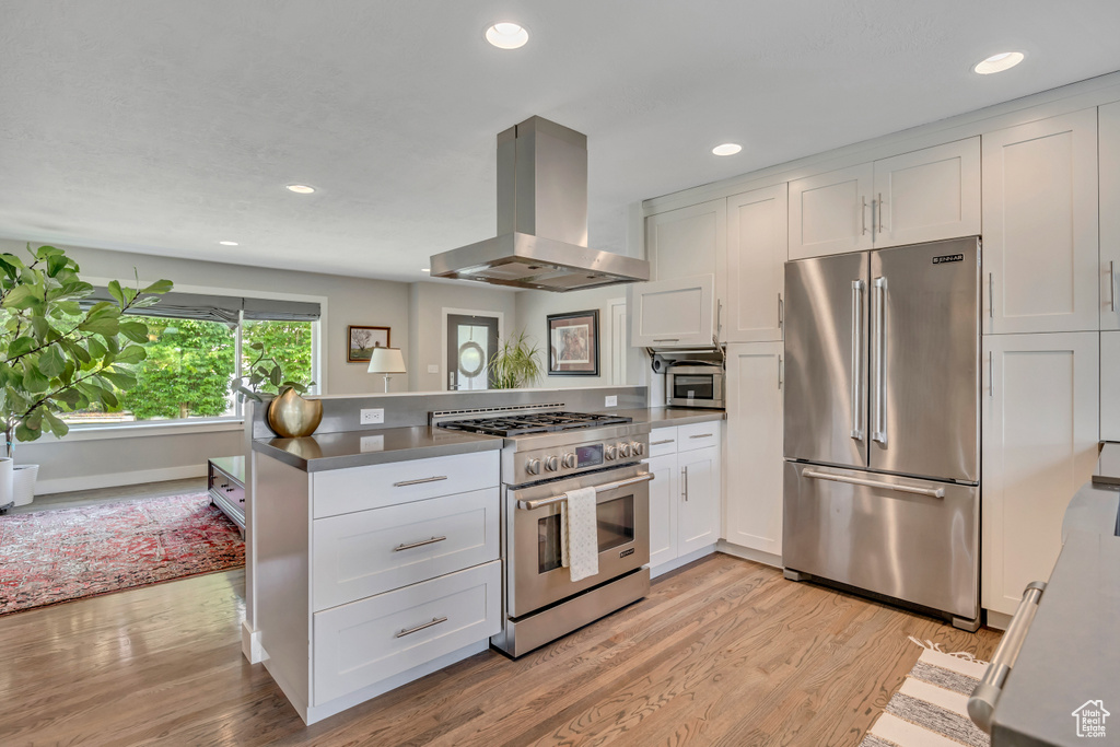 Kitchen with high quality appliances, island range hood, white cabinetry, light wood-style floors, and recessed lighting