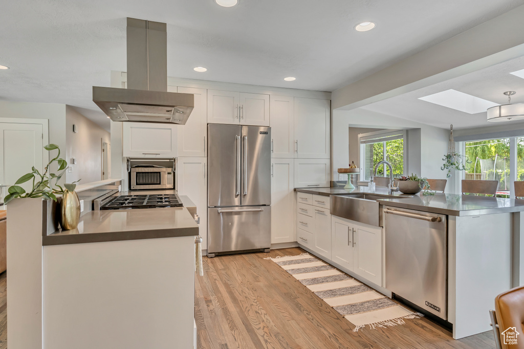 Kitchen featuring appliances with stainless steel finishes, island exhaust hood, a peninsula, light wood-type flooring, and white cabinets