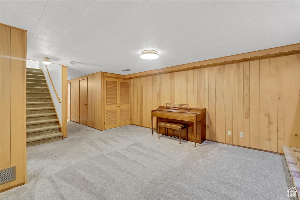 Finished below grade area featuring light colored carpet, stairs, and wooden walls