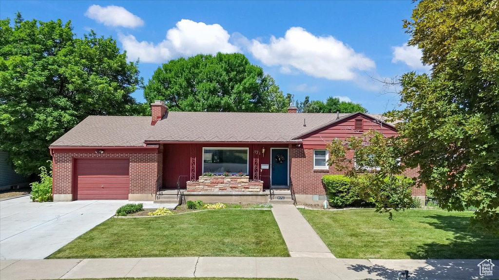 Ranch-style house with a garage, a chimney, driveway, brick siding, and a front lawn