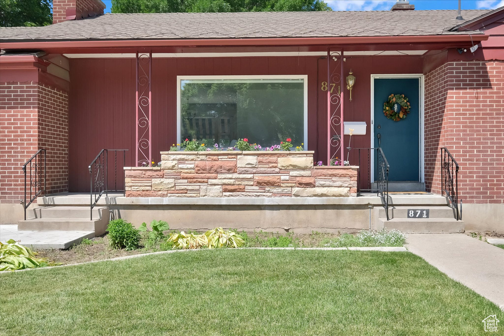 Entrance to property with a chimney, brick siding, a lawn, and a shingled roof