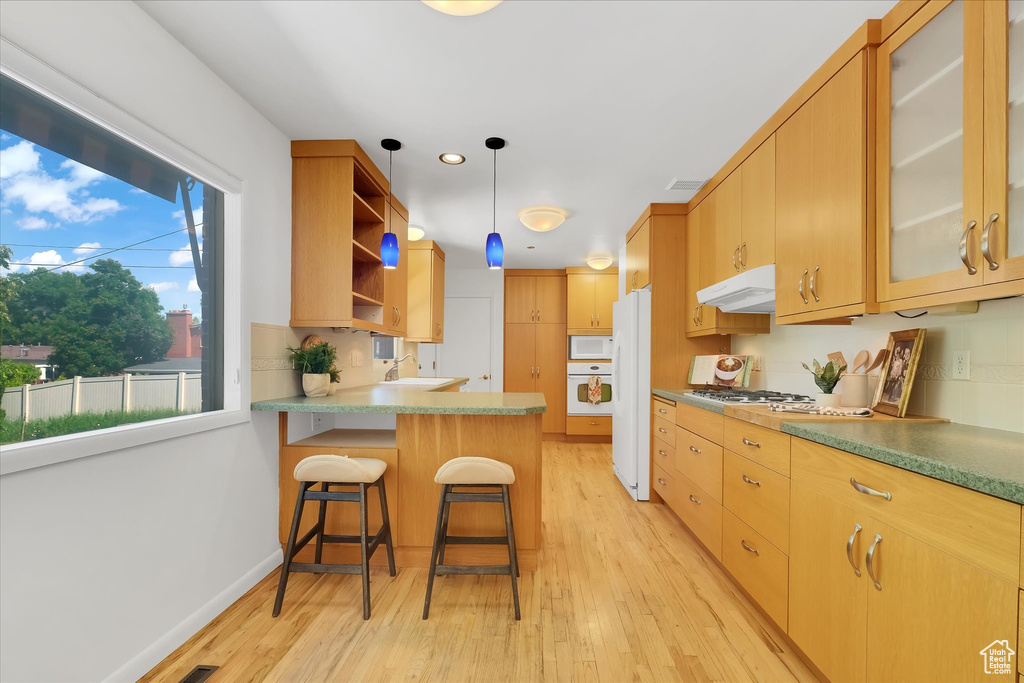 Kitchen with white appliances, light wood-type flooring, a peninsula, open shelves, and under cabinet range hood