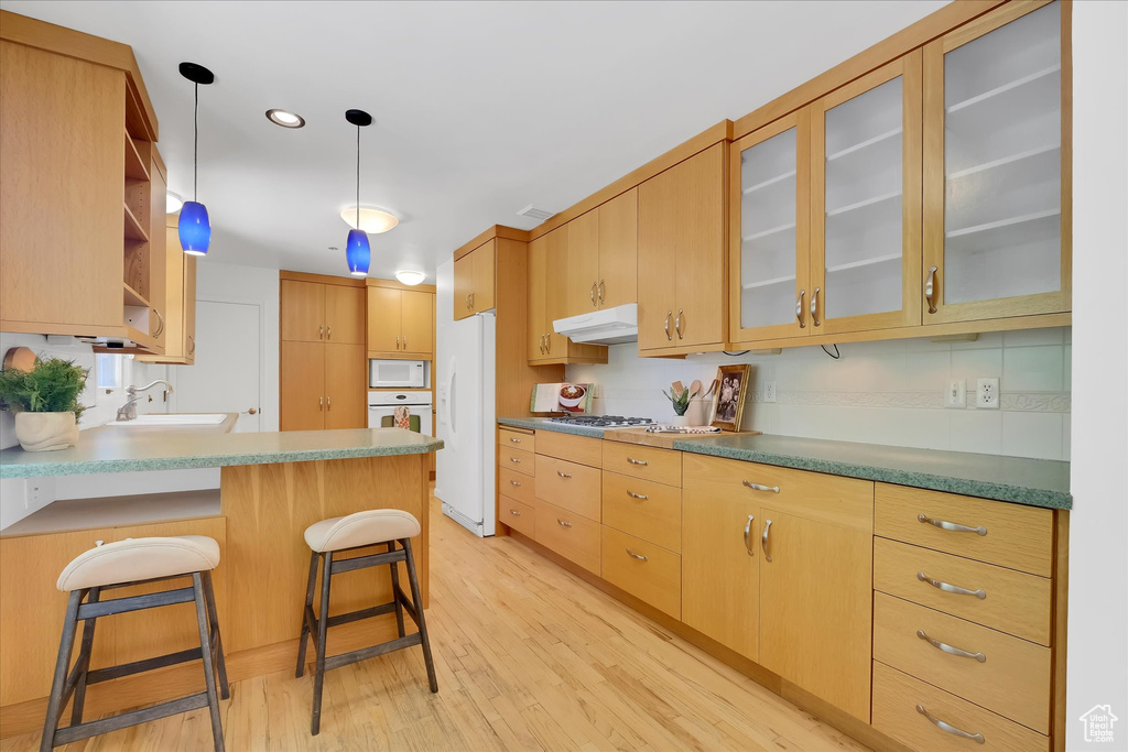 Kitchen featuring white appliances, under cabinet range hood, light wood-style flooring, a peninsula, and open shelves