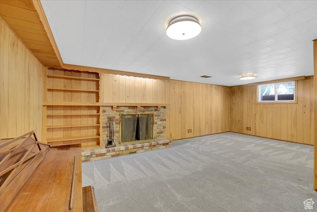 Unfurnished living room featuring wooden walls, carpet flooring, and a fireplace