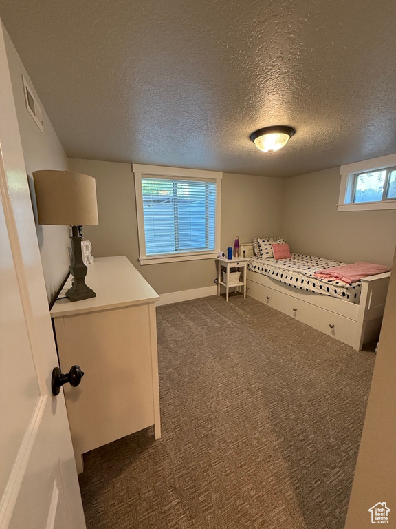 Unfurnished bedroom with a textured ceiling, dark carpet, and multiple windows