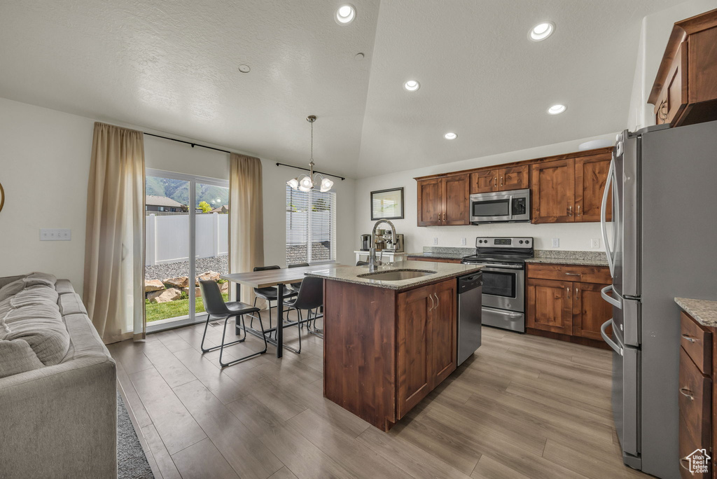 Kitchen featuring appliances with stainless steel finishes, open floor plan, a chandelier, light wood-style flooring, and recessed lighting