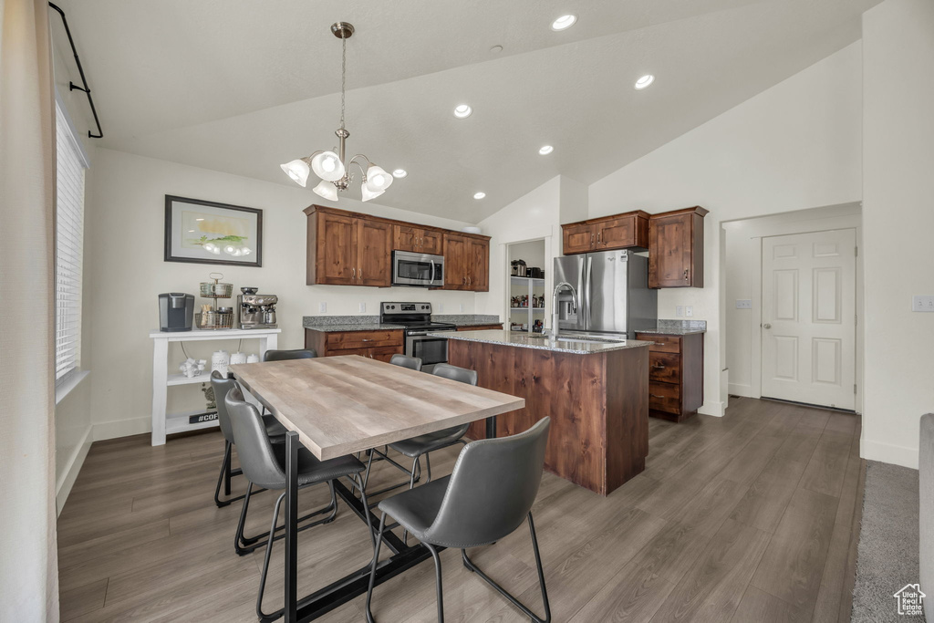 Kitchen featuring appliances with stainless steel finishes, a kitchen island with sink, a chandelier, high vaulted ceiling, and dark wood-style floors
