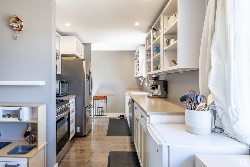 Kitchen with stainless steel appliances, light wood-style flooring, light countertops, white cabinetry, and recessed lighting