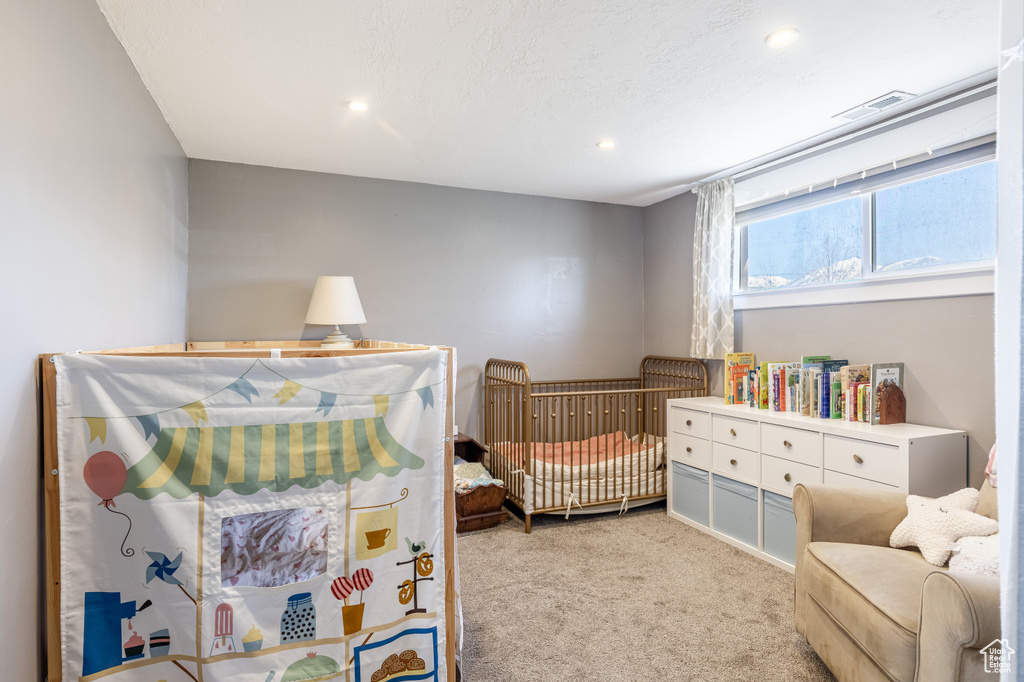 Carpeted bedroom with recessed lighting and a nursery area