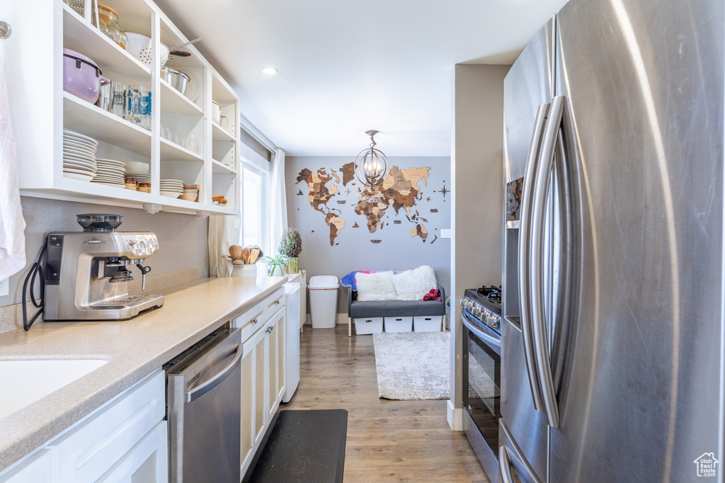 Kitchen with stainless steel appliances, a chandelier, light wood finished floors, white cabinets, and open shelves