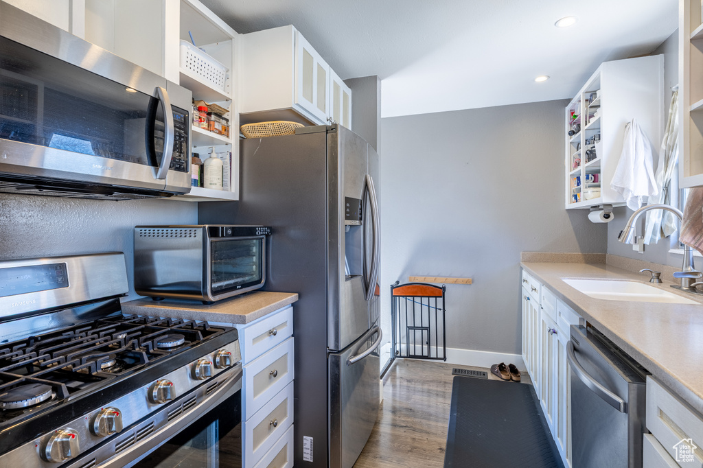Kitchen featuring stainless steel appliances, open shelves, white cabinets, wood finished floors, and light countertops