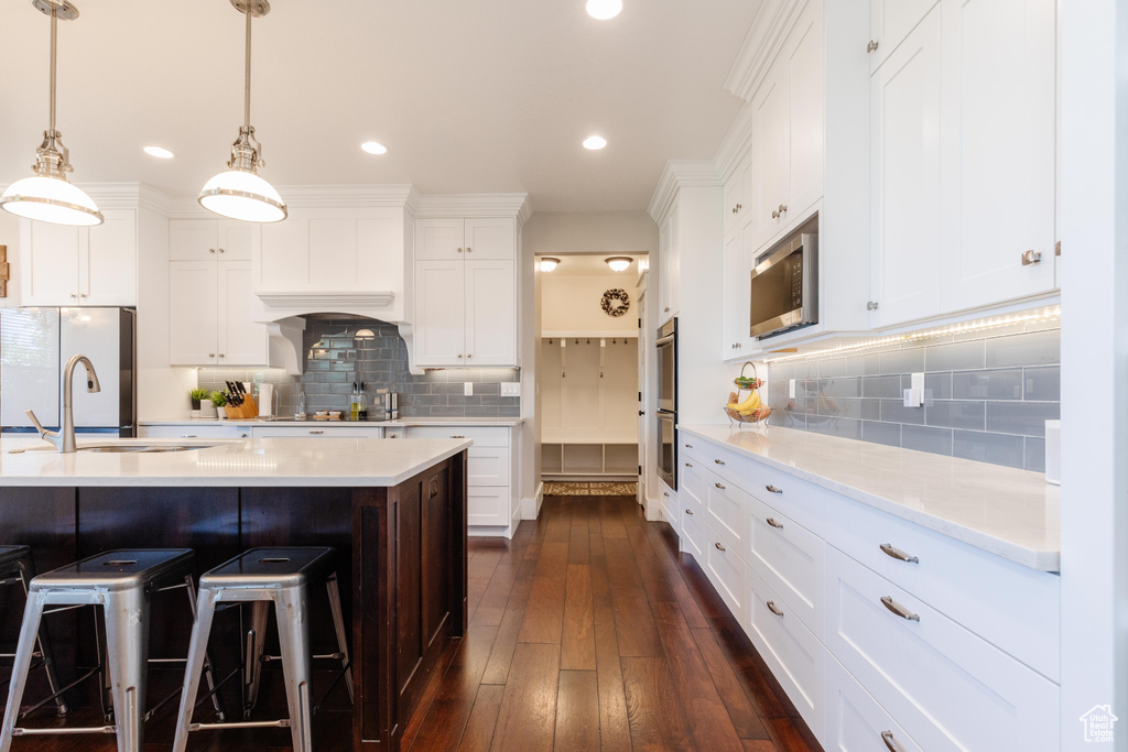 Kitchen with stainless steel appliances, decorative backsplash, white cabinets, a breakfast bar, and recessed lighting
