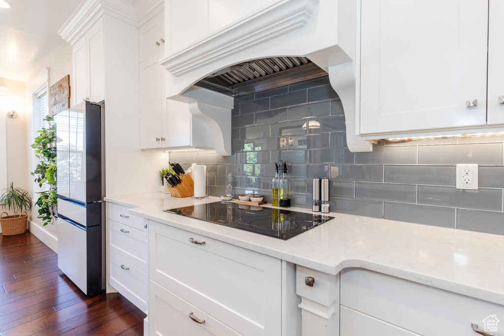 Kitchen with black electric cooktop, custom range hood, freestanding refrigerator, and decorative backsplash