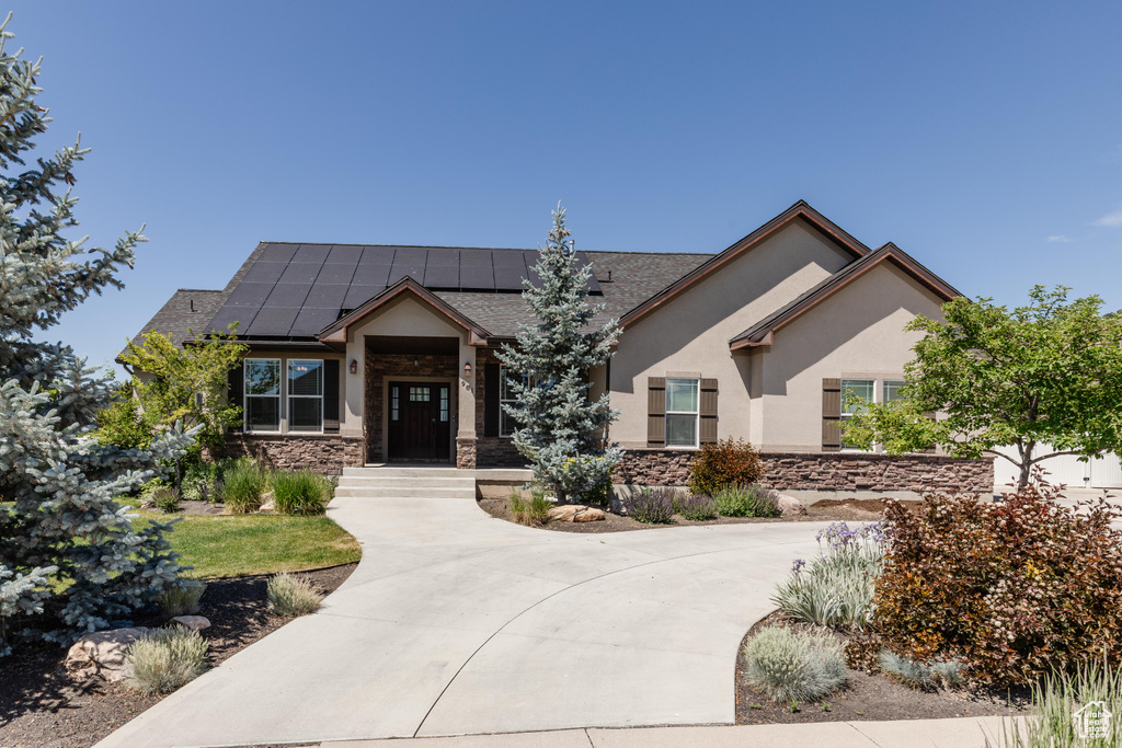 View of front of home featuring stone siding, stucco siding, and roof mounted solar panels