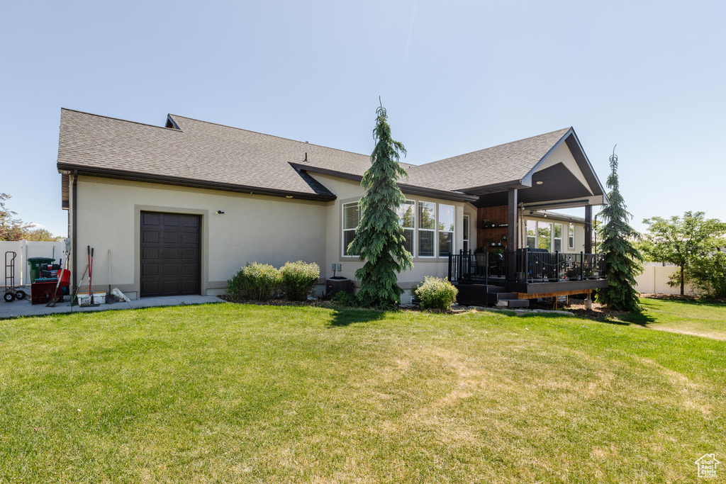 View of front of house featuring a front yard, a deck, roof with shingles, stucco siding, and a garage