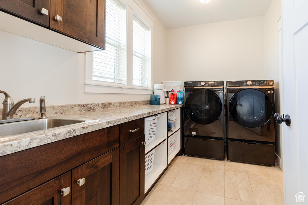 Laundry area featuring independent washer and dryer, light tile patterned floors, and cabinet space