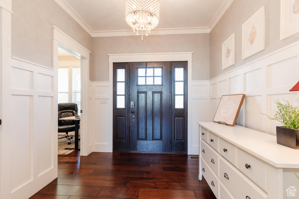 Foyer entrance featuring a decorative wall, dark wood-type flooring, a chandelier, wainscoting, and ornamental molding