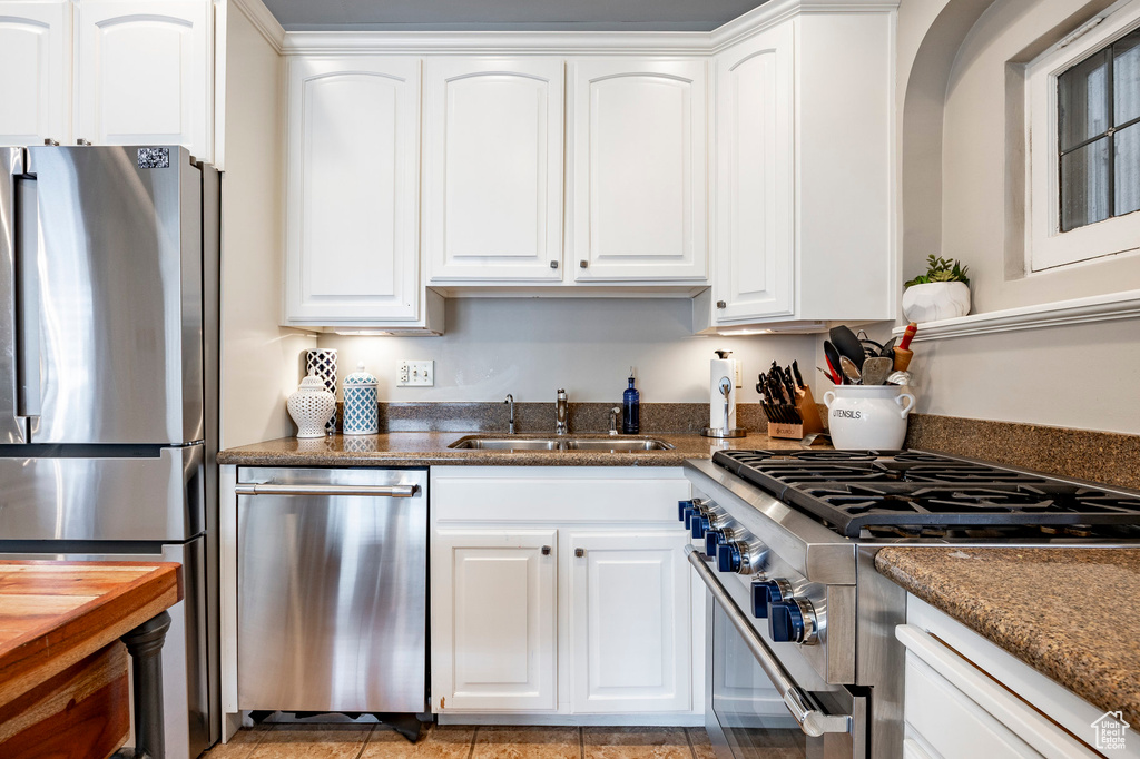 Kitchen featuring appliances with stainless steel finishes, a sink, white cabinets, and dark stone countertops