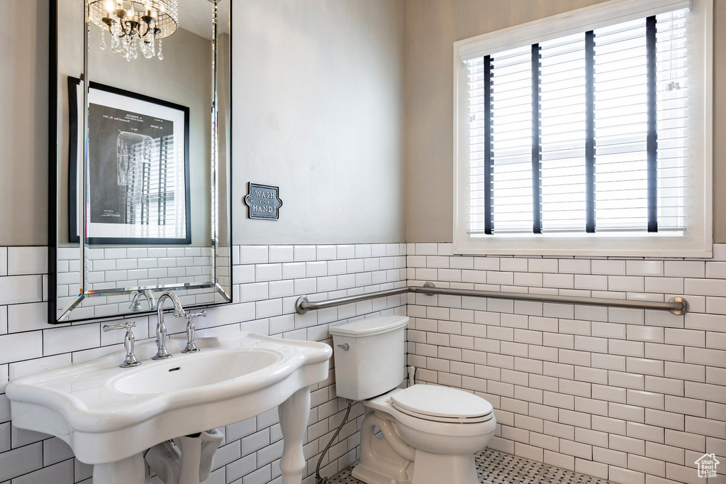 Bathroom with toilet, tile walls, wainscoting, a sink, and a chandelier
