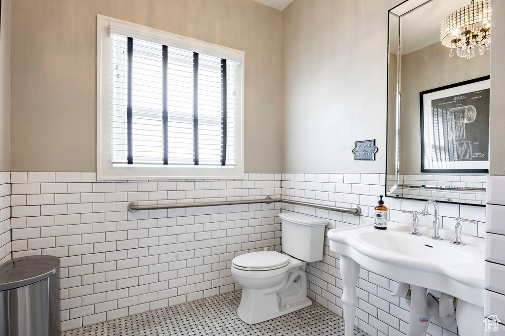 Bathroom featuring tile walls, a wainscoted wall, toilet, tile patterned flooring, and a chandelier