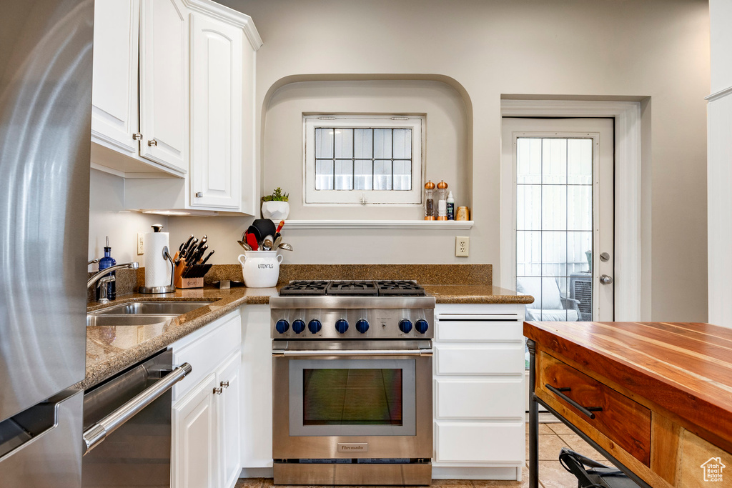 Kitchen featuring appliances with stainless steel finishes, a sink, dark stone countertops, white cabinets, and light tile patterned floors