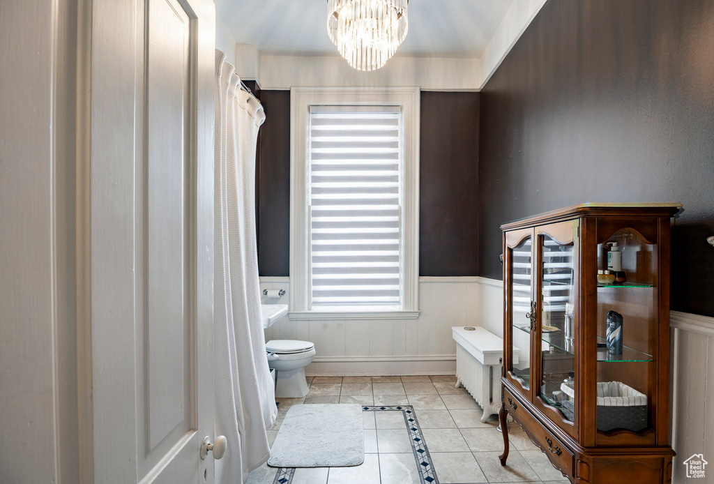 Bathroom with inlaid floor details, a wainscoted wall, toilet, a chandelier, and tile patterned floors