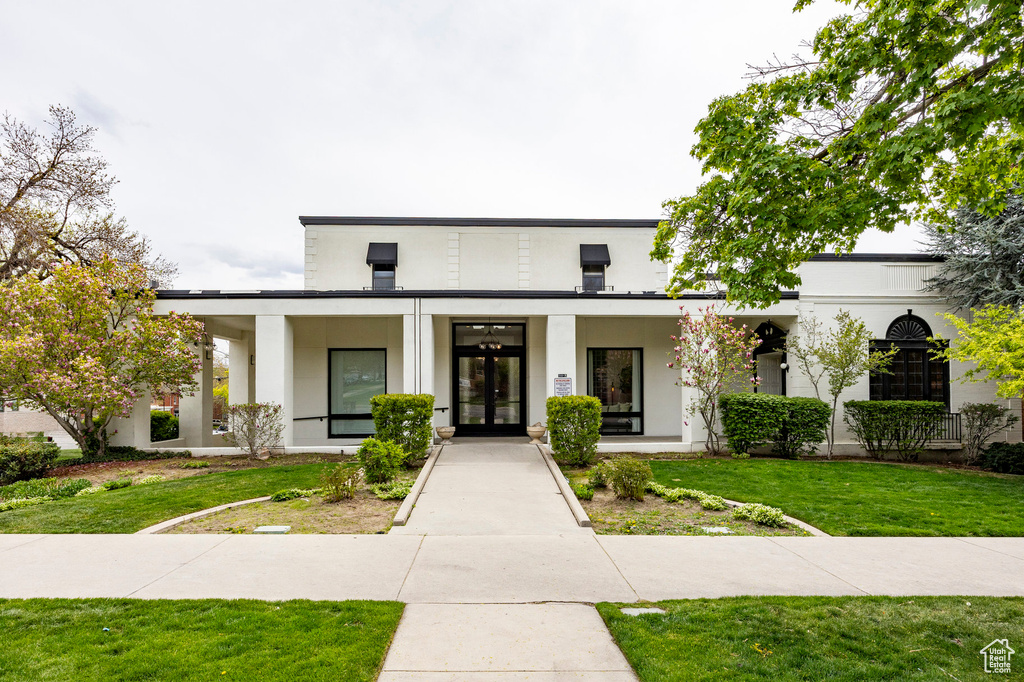 View of front facade with french doors, stucco siding, and a front lawn