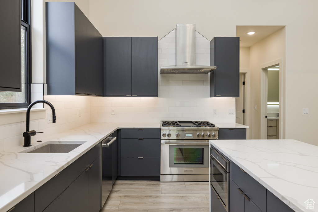 Kitchen with wall chimney exhaust hood, stainless steel appliances, a sink, decorative backsplash, and recessed lighting