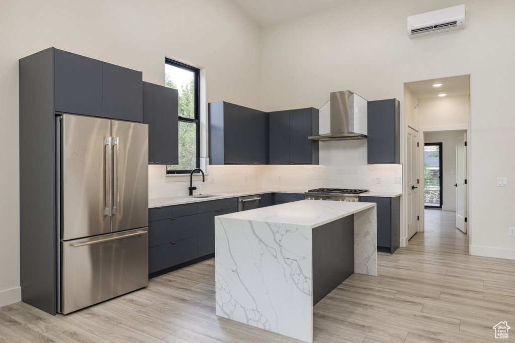 Kitchen with high end fridge, wall chimney exhaust hood, a wall unit AC, a high ceiling, and a sink