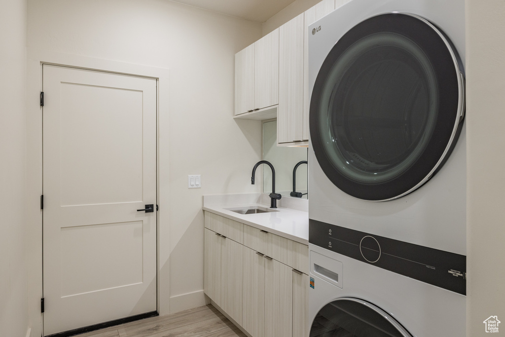 Laundry area with estacked washer and dryer, cabinet space, light wood-type flooring, and baseboards