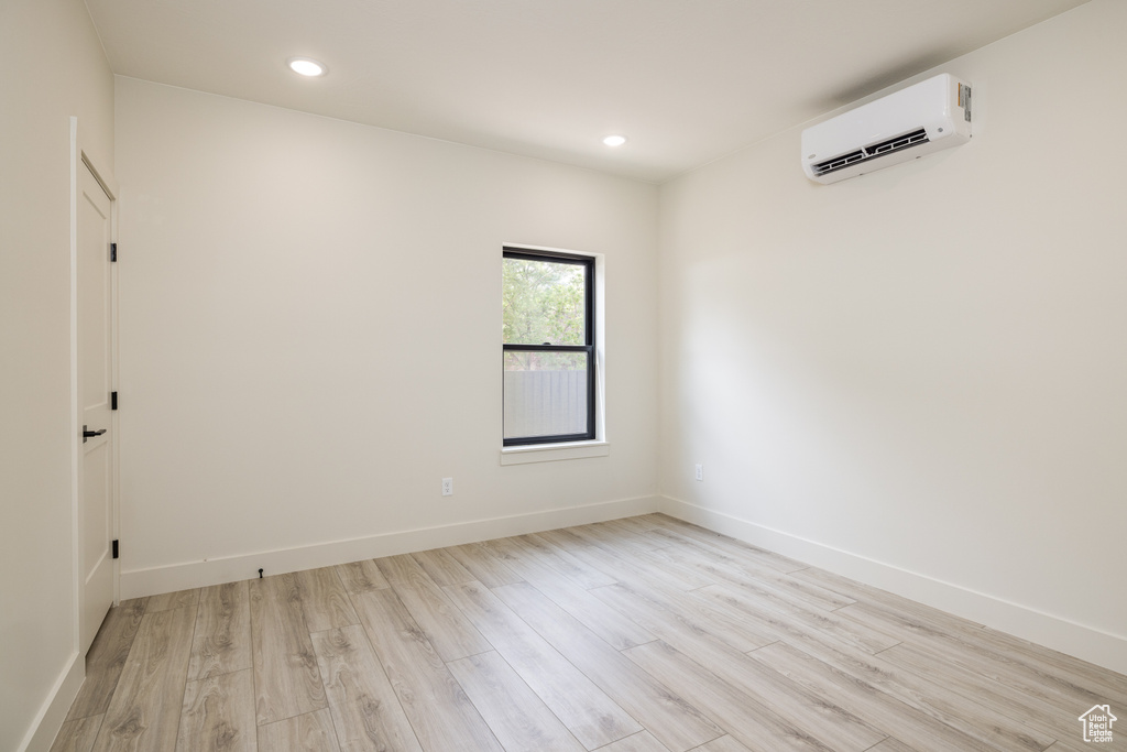 Empty room with an AC wall unit, light wood-type flooring, recessed lighting, and baseboards
