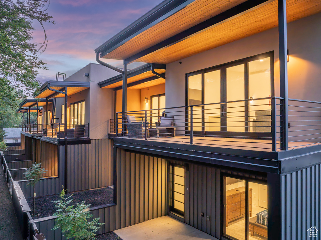 Back of property at dusk with stucco siding, a balcony, and board and batten siding