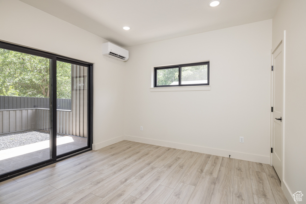Empty room with a wall mounted air conditioner, light wood-type flooring, recessed lighting, and baseboards